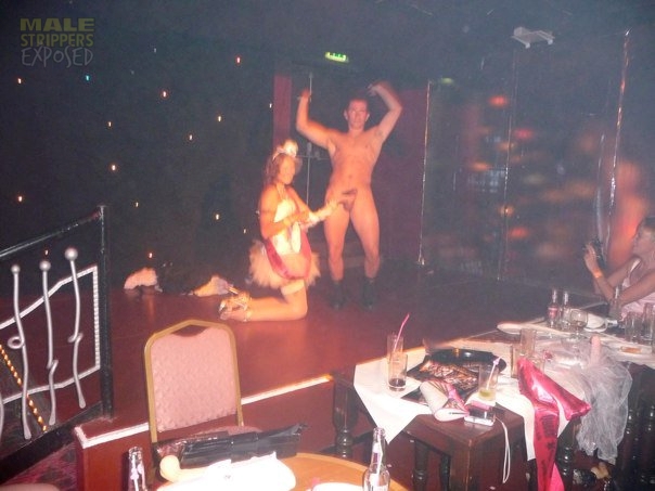 A woman holds a naked male stripper's penis on her hand