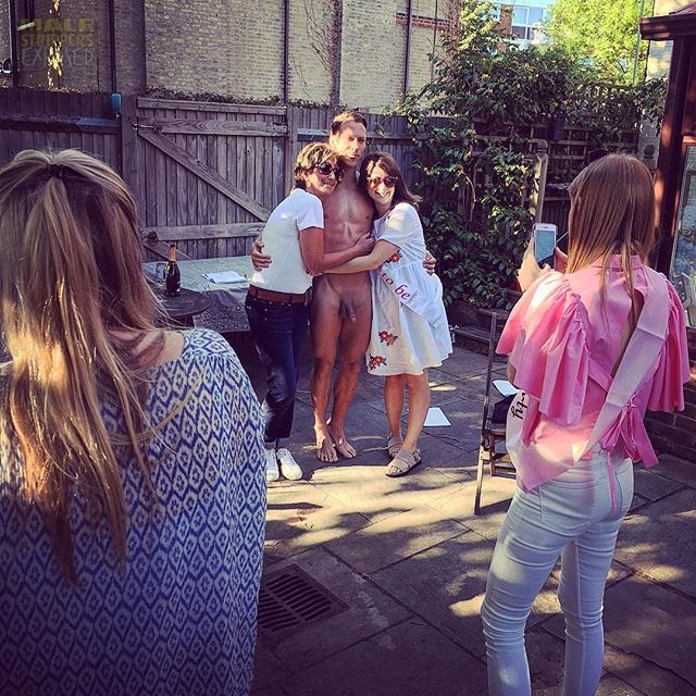 A naked male stripper poses with women at a garden party