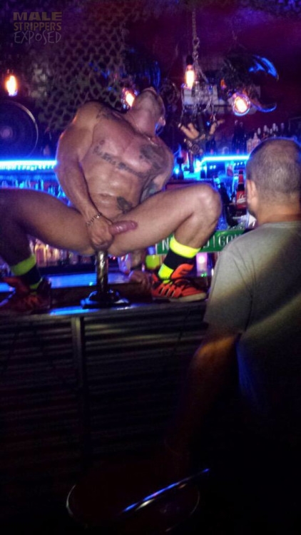 A naked male stripper sitting on the bar putting a dildo up his ass